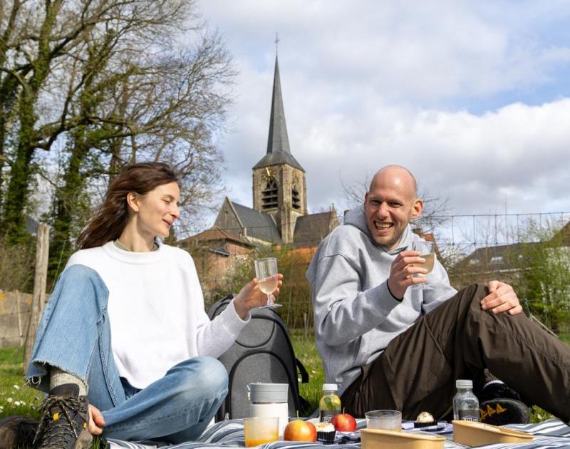 Twee mensen op een picknickdeken met kerktoren Sint-Martens-Bodegem op de achtergrond