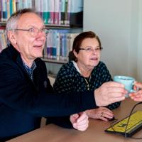 twee senioren krijgen hulp bij computer én een kopje koffie